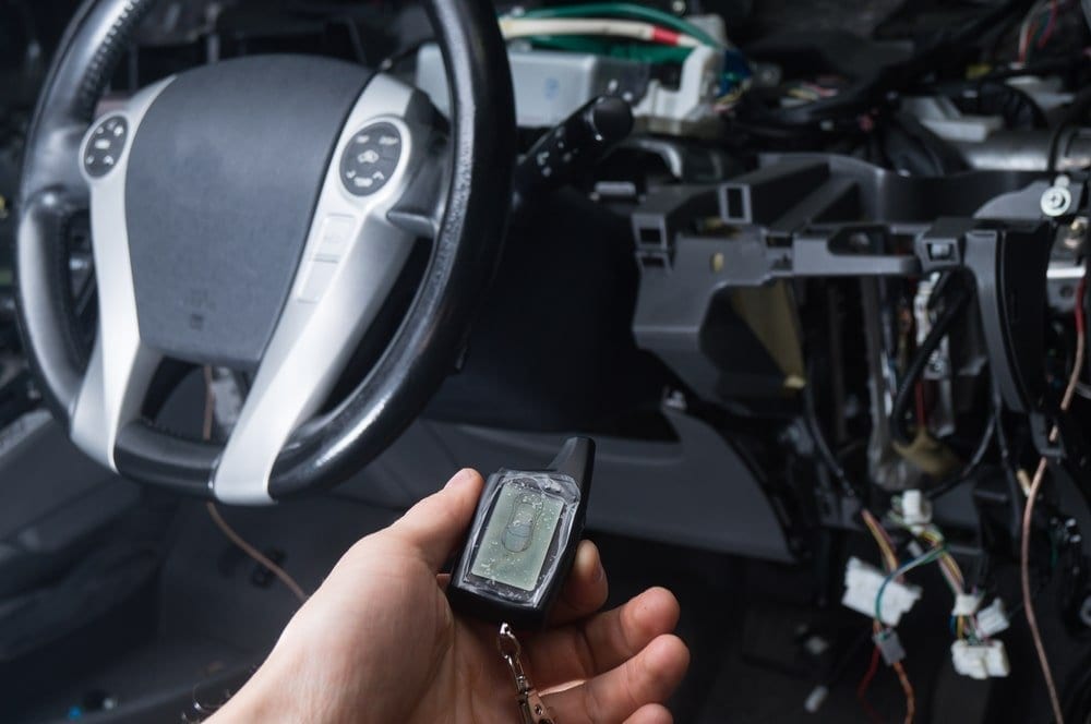 installing a car alarm or remote start with exposed wires and remote in hand