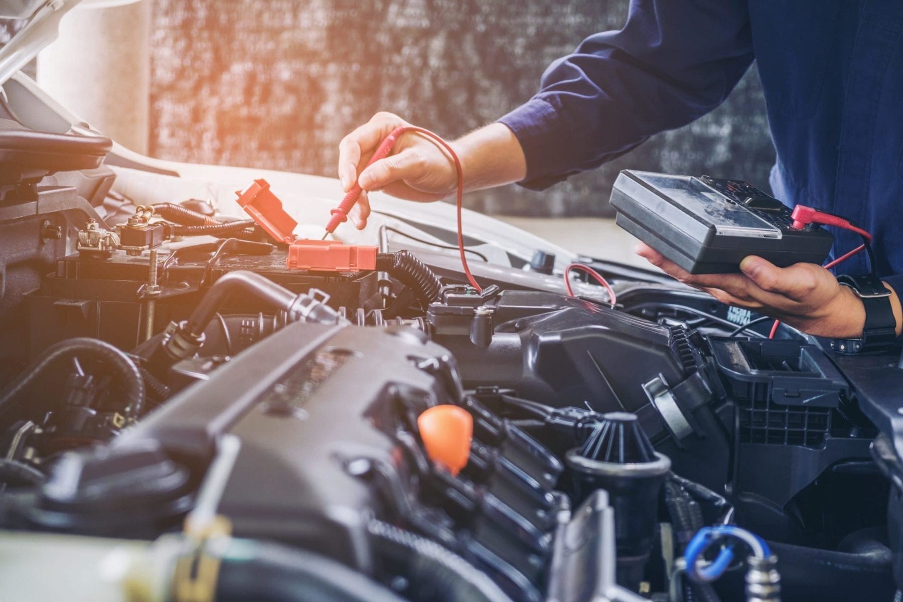 Mechanic checking voltage of dead battery in car with voltmeter