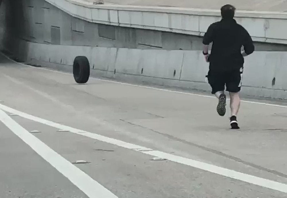man chasing runaway tire down the street