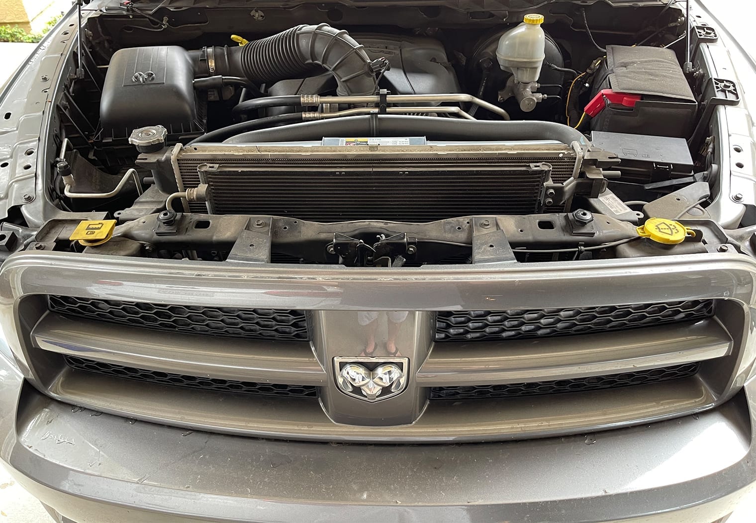 Image of the 2012 ram 1500 engine bay with the trim cover removed to get access to the grill bolts before removing headlights