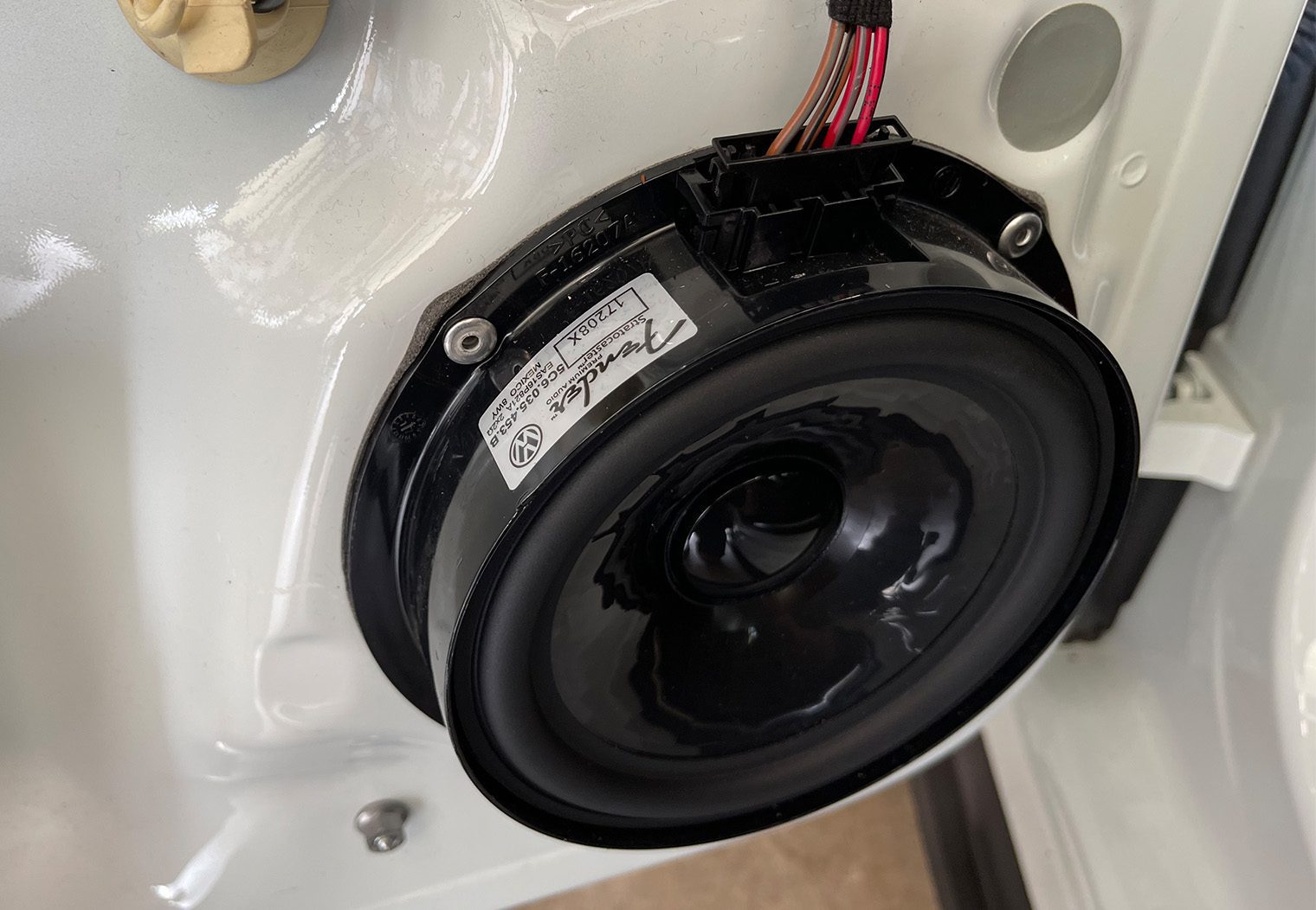 Closeup picture of the OEM Fender speaker in a 2018 VW GTI MK7.5 to showcase the rivets and the wire harness