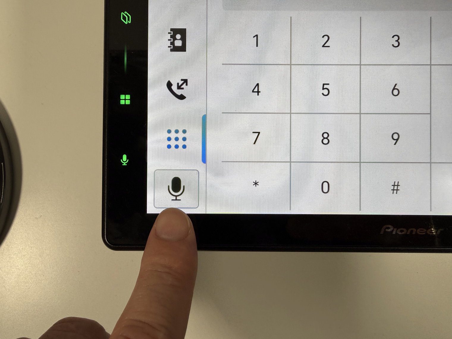 Close-up of a finger at the on-screen mic button beside the Pioneer DMH-WT8000NEX phone keypad